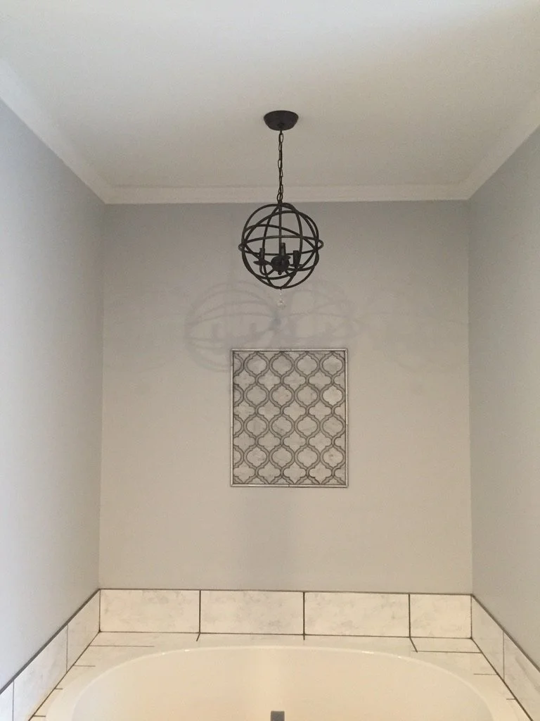 Bathroom corner with light gray walls, decorative wall piece, tiled ledge, and a black globe-style pendant light fixture hanging from the ceiling.