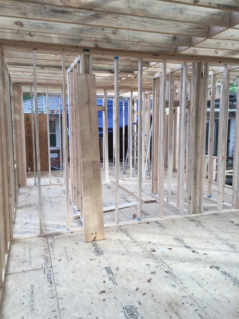 Indoor view of a construction site with wooden framing and plywood subflooring, showing the early stages of building a room or house.