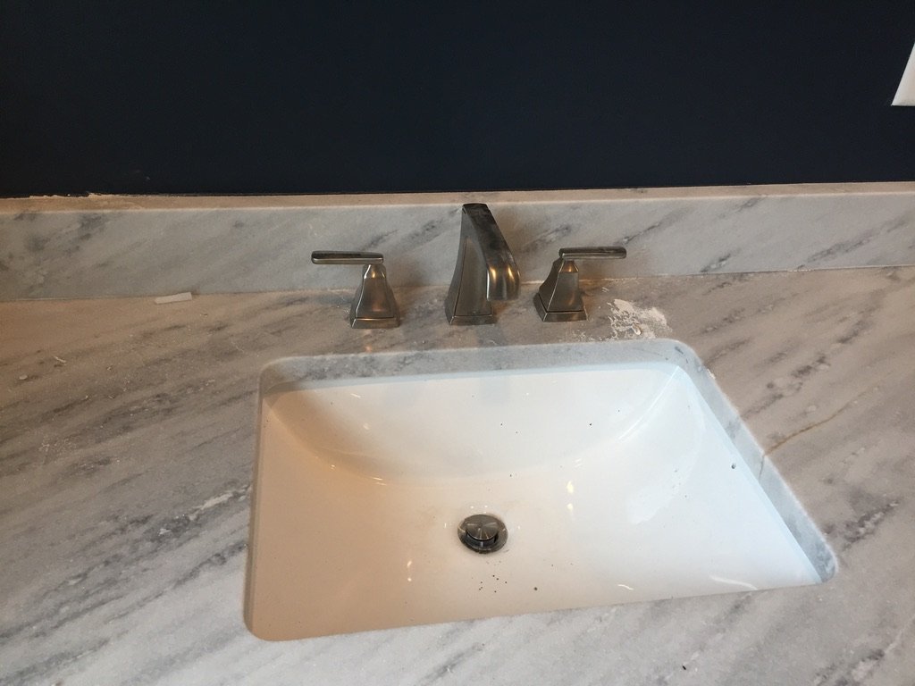 Bathroom sink with marble countertop and silver faucet set against dark wall.