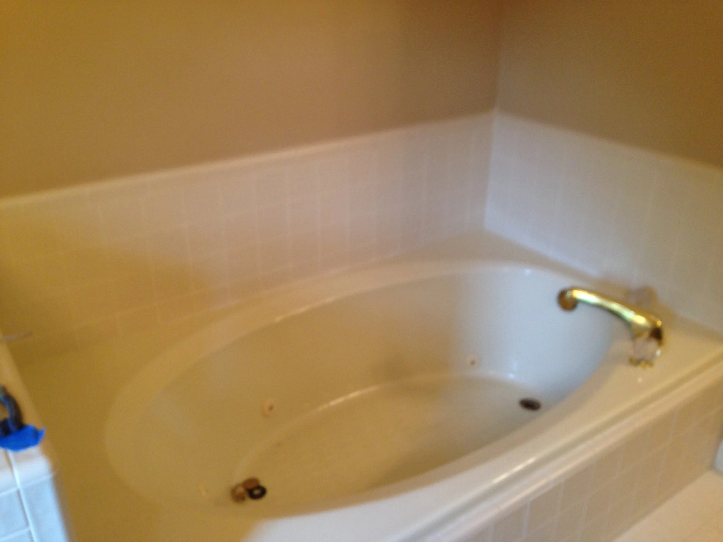 The image shows a beige-colored wall with a corner on the top right. There is a shiny brass-colored handle or fixture attached to the wall on the right side. The overall image is slightly blurry.