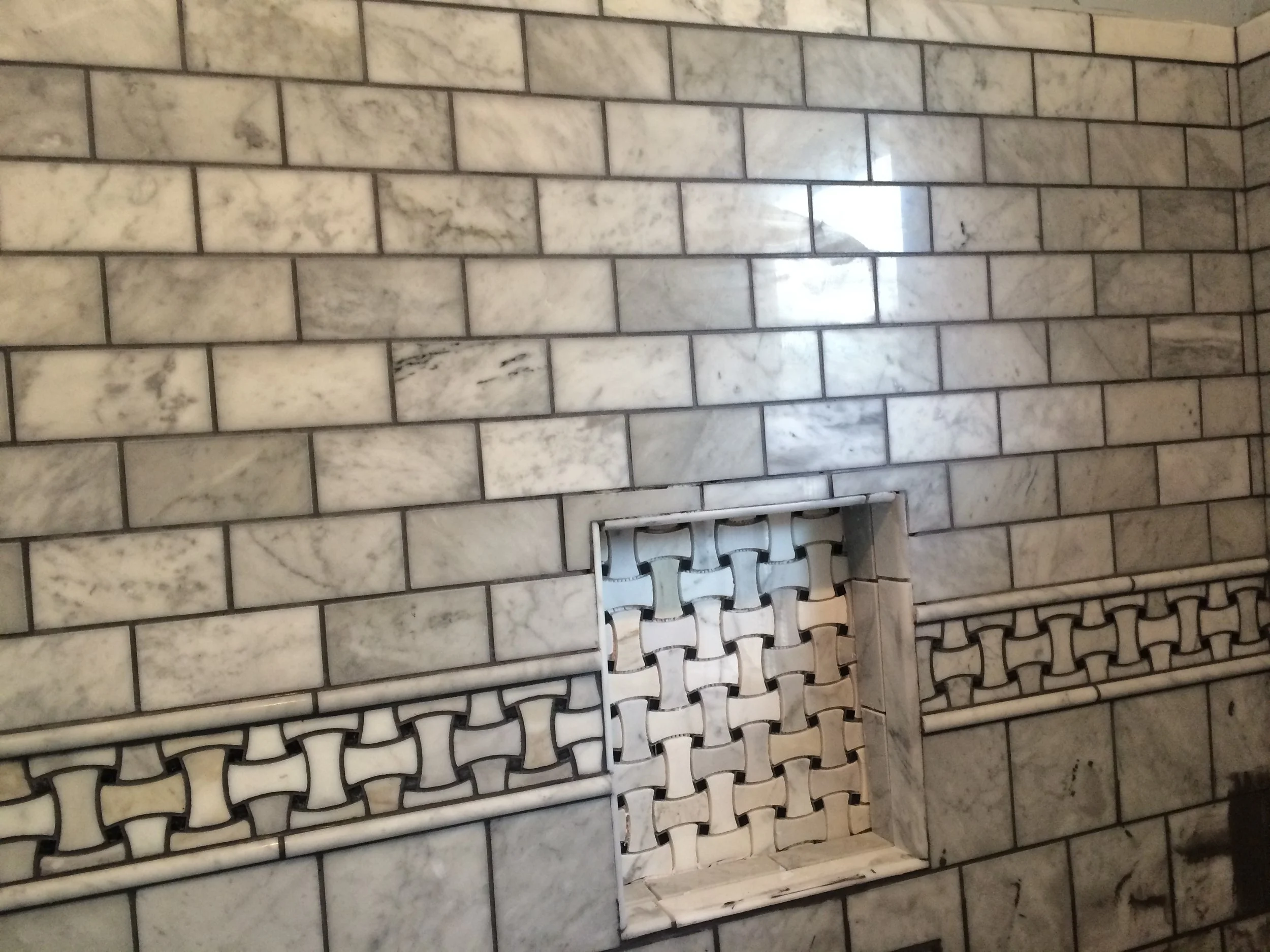 Close-up of a marble tiled wall with a decorative metal grate near the floor.