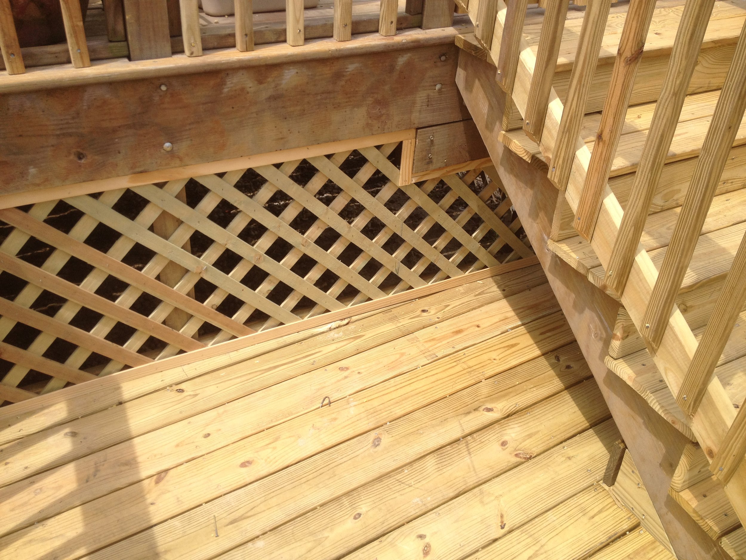 A wooden deck with lattice underneath and a set of stairs with railing on the right side.