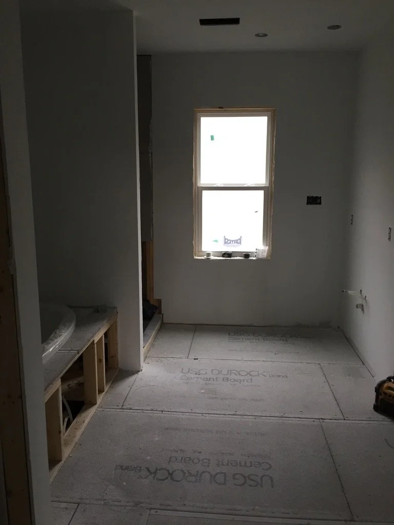 Interior of a room under construction with drywall installed, a window, and floor sheathing. There is built-in cabinetry framing on the left and some electrical outlets and wiring visible.