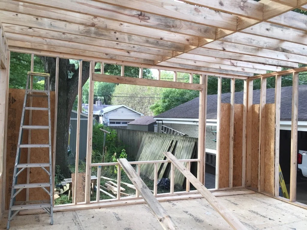 Construction site with wooden framing for a new building, ladder leaning against the wall, and construction material scattered on the floor.