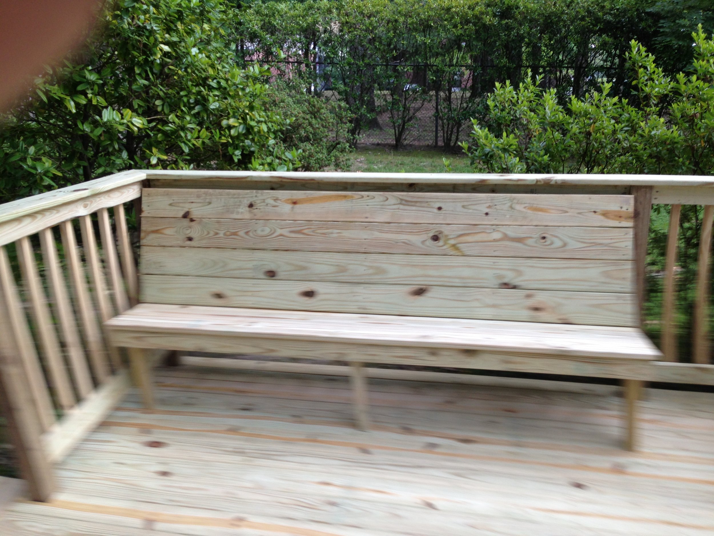 A view from a wooden porch or deck overlooking lush green trees and bushes, with a chain-link fence in the background.