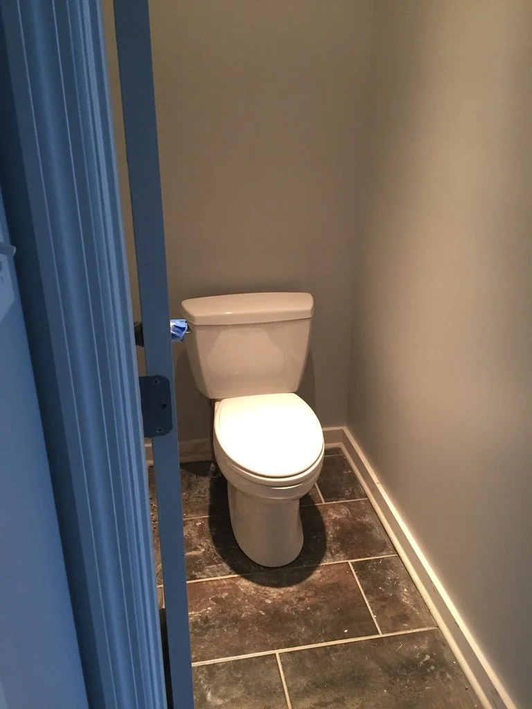 A small bathroom with a white toilet against a gray wall, dark tile floor, and a blue door partially open.