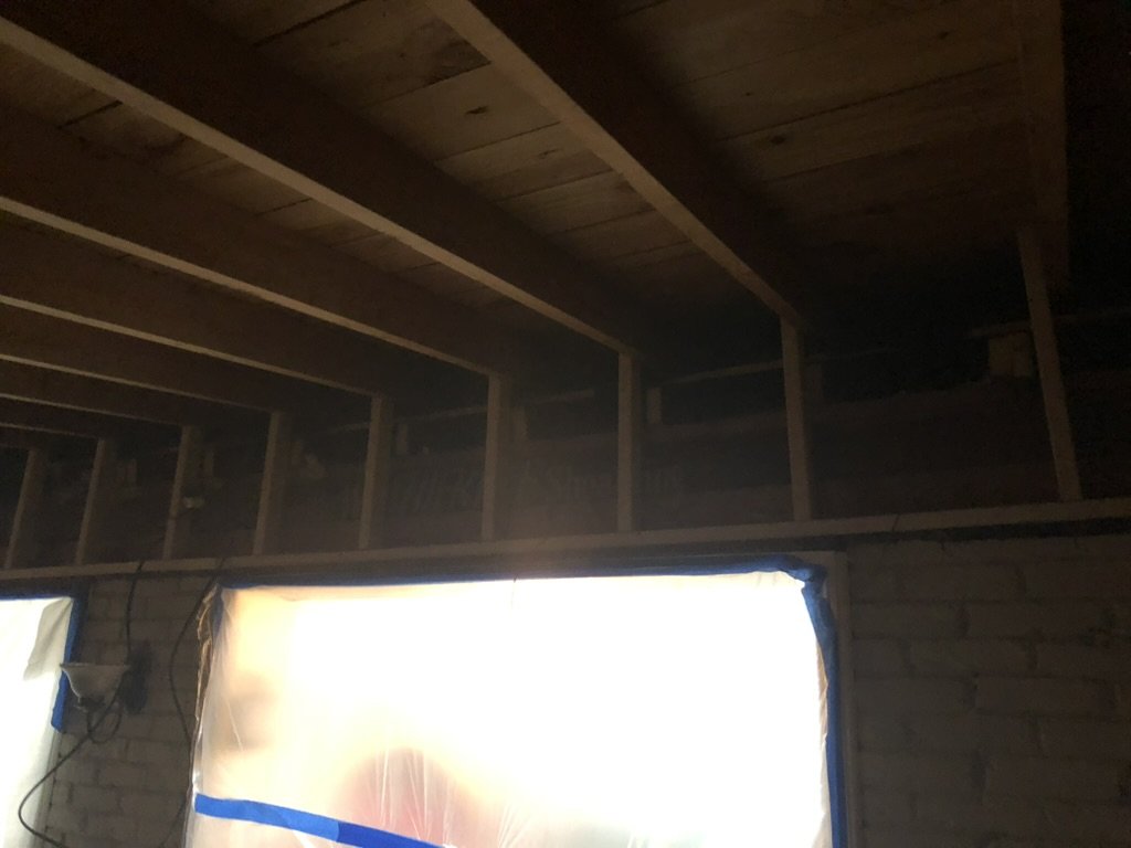 Interior of a house under construction, showing exposed wooden beams and framing above a window with protective plastic.