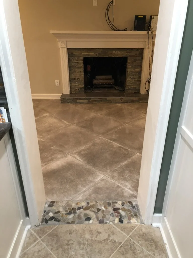 View of a living room with a fireplace framed with white molding and a stone interior, with a small raised hearth, and a wall with electronic devices and cables on top.
