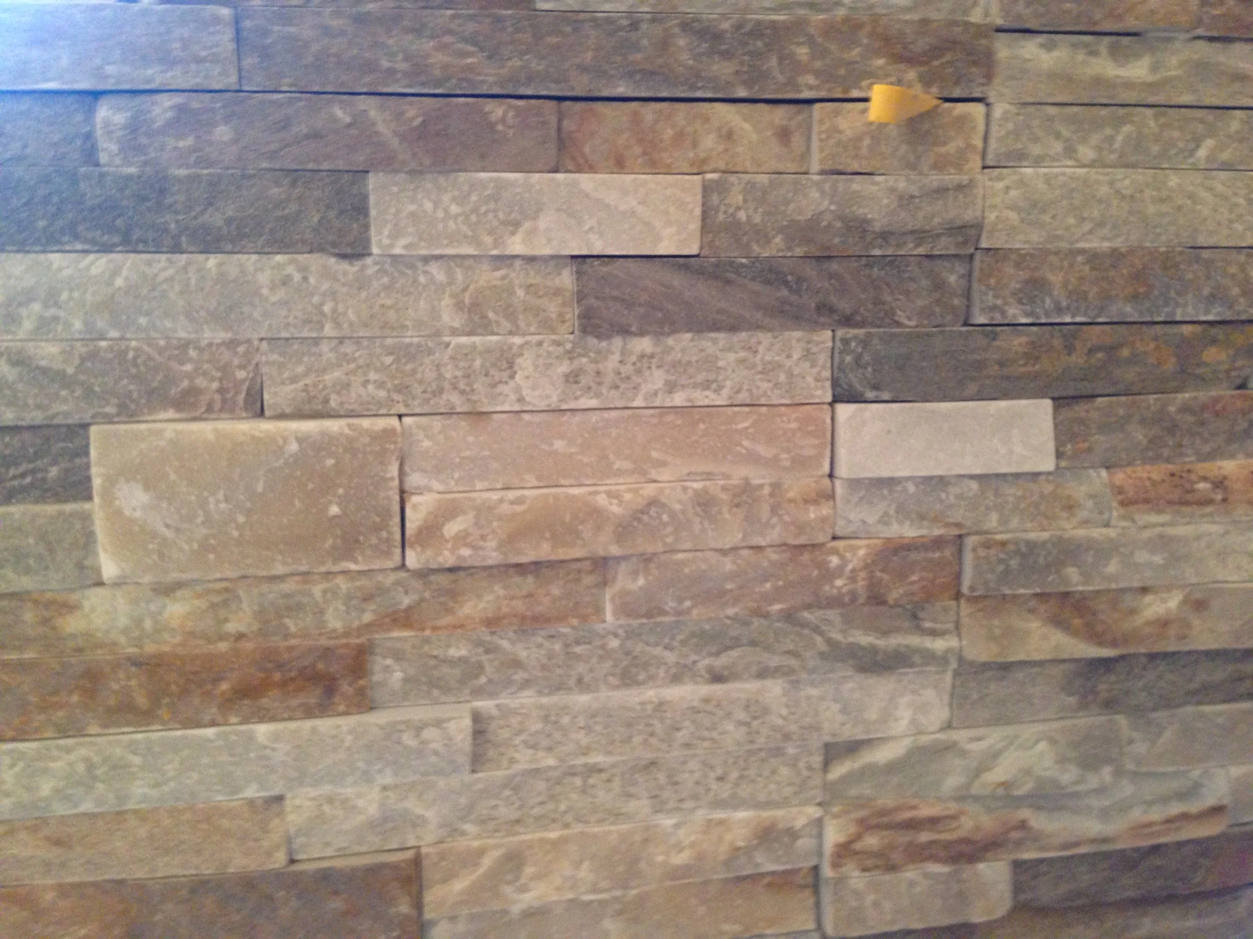 A wall made of rectangular stone tiles in various earthy tones, arranged in a horizontal pattern.