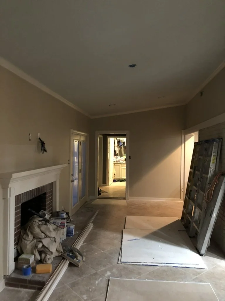 Living room under renovation with construction materials, a ladder, and tools near a fireplace.