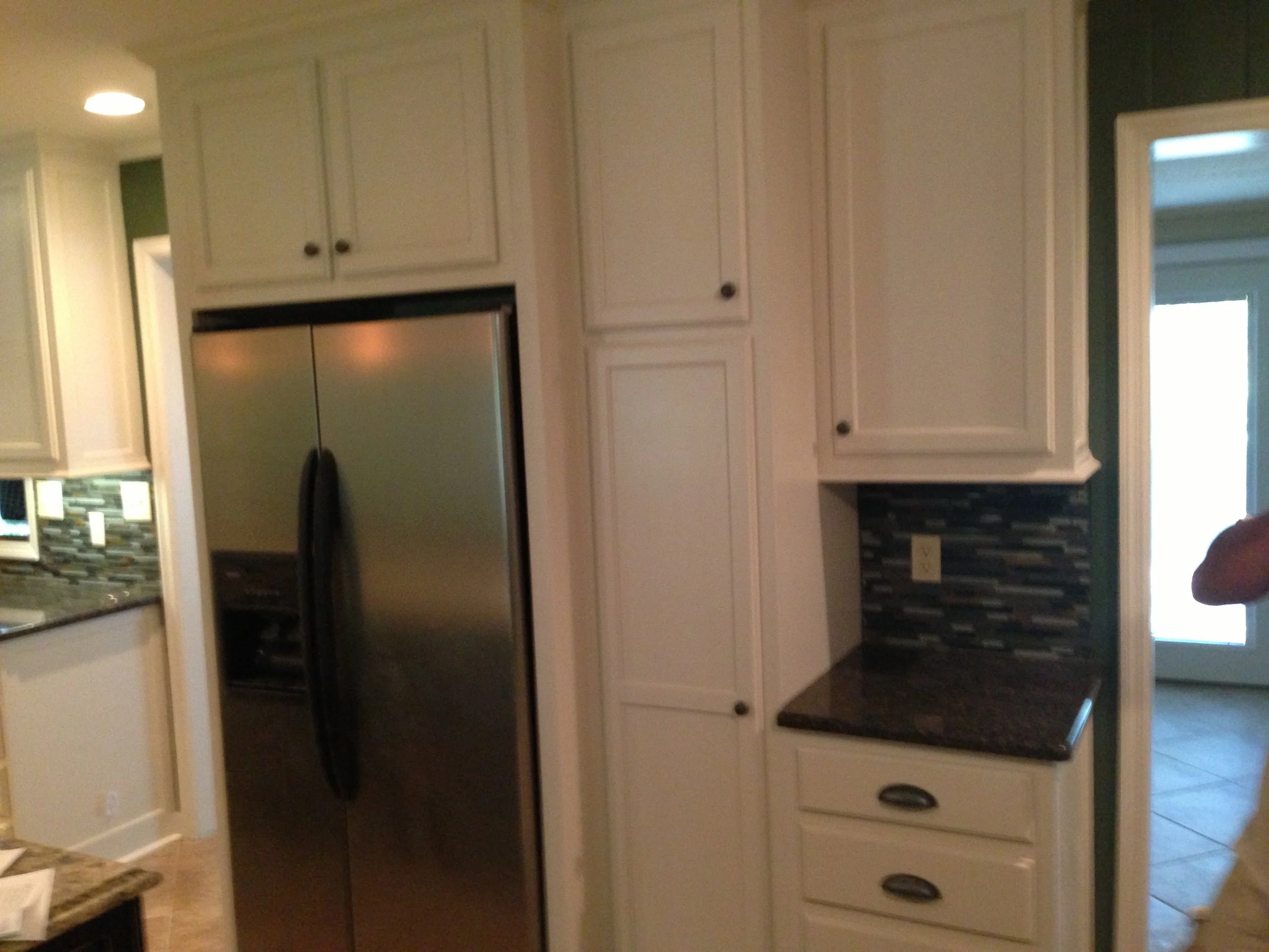 Kitchen with white cabinets, black countertop, stainless steel refrigerator, and tiled backsplash.