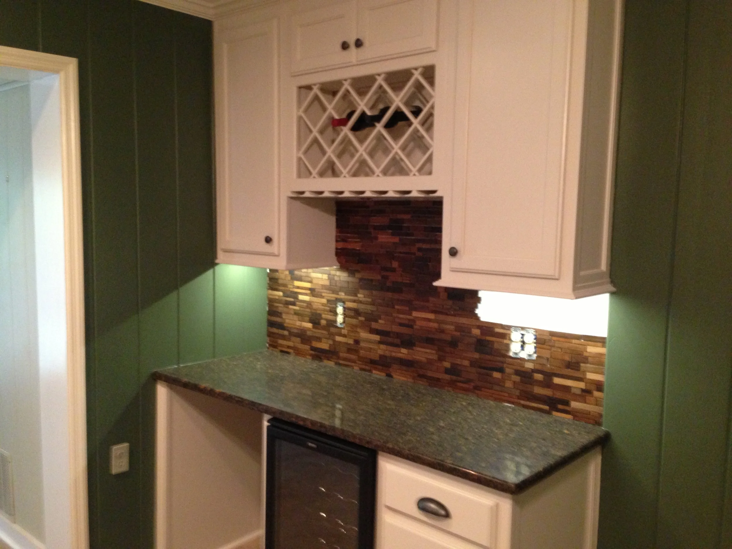 Kitchen with green walls, beige cabinets, a wine rack, brick backsplash, granite countertop, and black appliances.