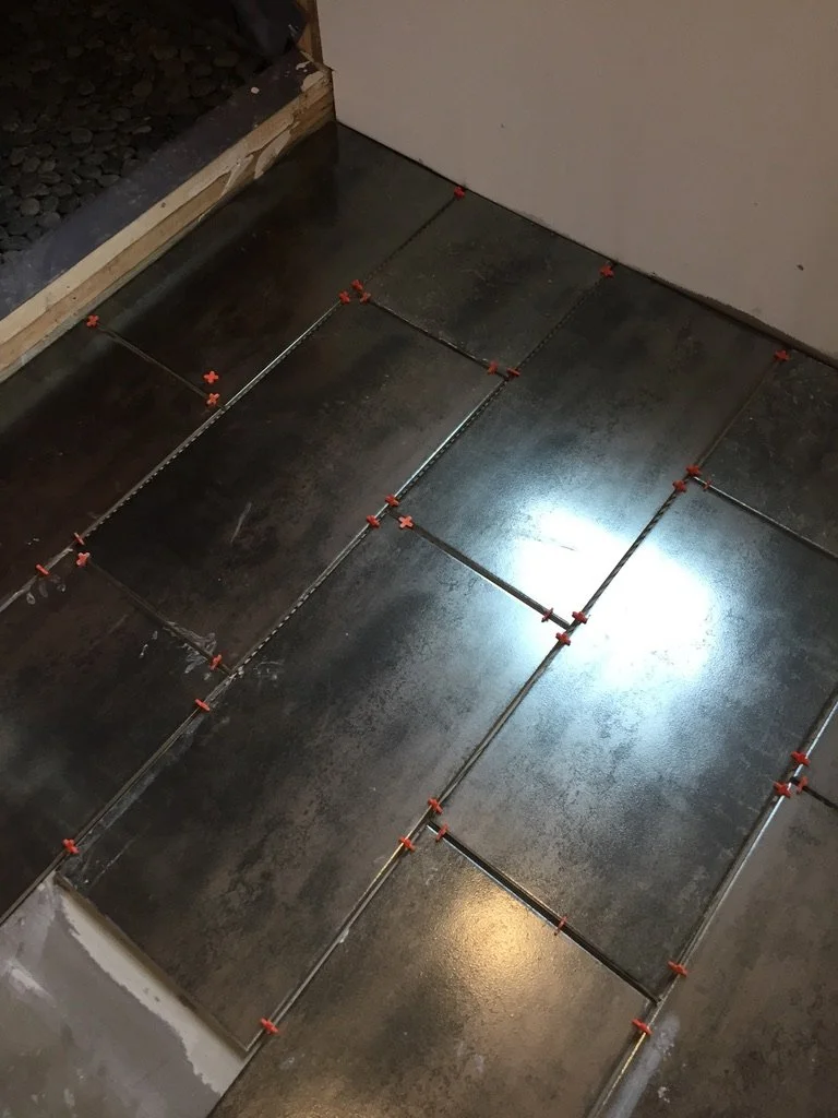 Installing dark-colored floor tiles with spacers visible between tiles for even grout lines.