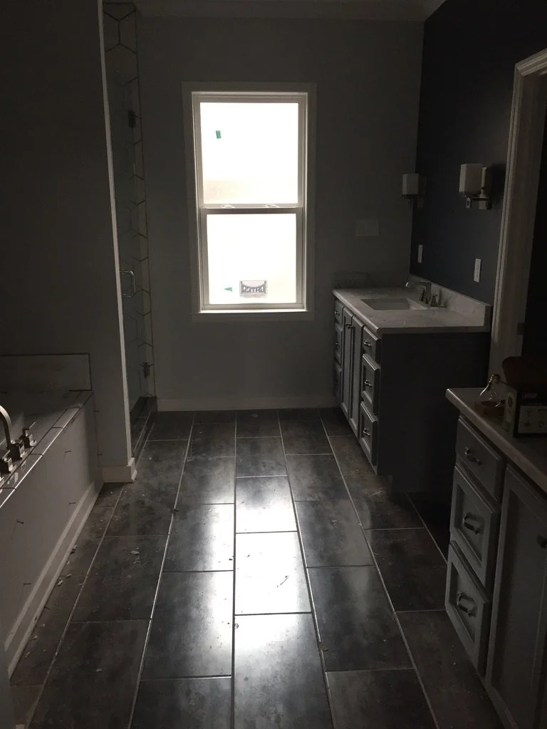 Interior of a kitchen under construction with dark tiles on the floor, a window on the back wall, and unfinished cabinetry.