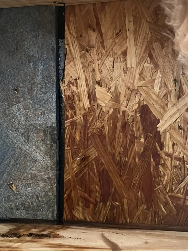 Close-up of a wall with gray particle board on the left and oriented strand board on the right.