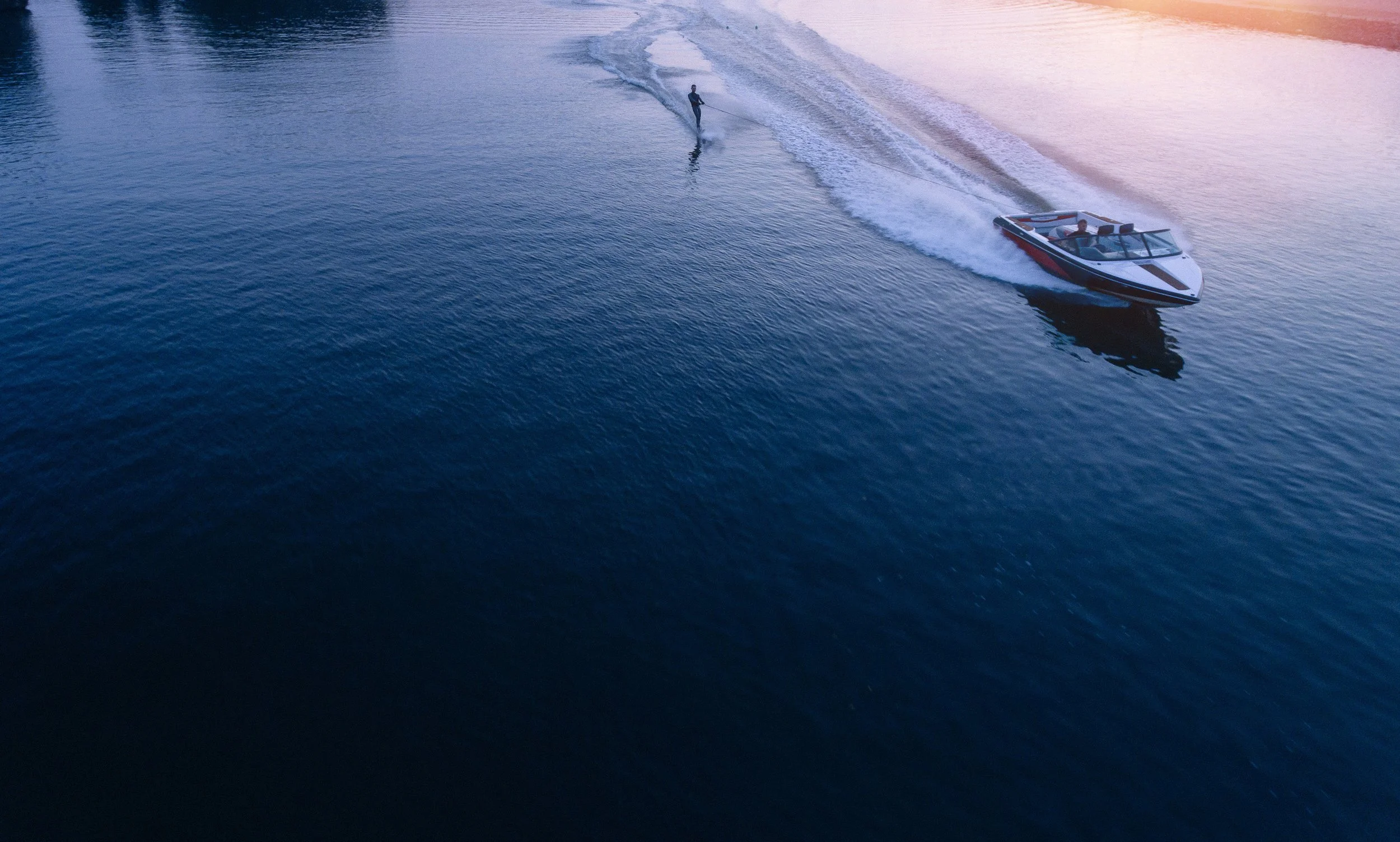 A person waterskiing behind a boat on a body of water during sunset.