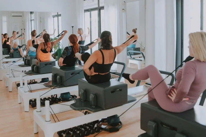 Group of women participating in a Pilates or fitness class using reformer machines in a bright studio.