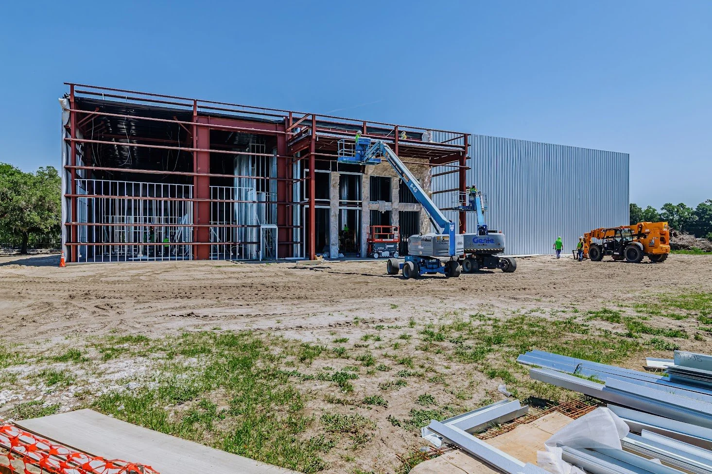 Construction site of a building with steel framework and partially installed exterior wall panels, with construction workers and equipment on site.