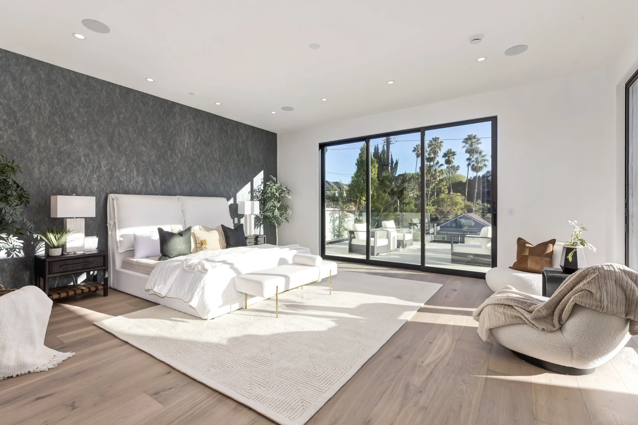 [home-additions] Primary bedroom with charcoal accent wall and glass doors to a private terrace, Encino custom home