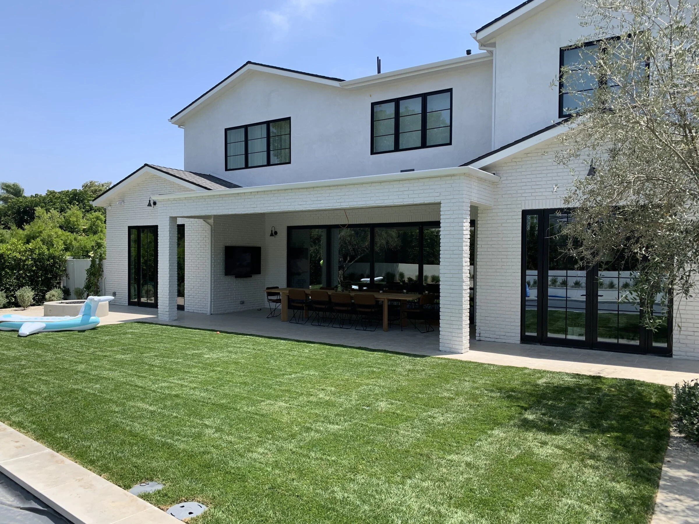 [hardscaping] Finished modern farmhouse backyard with a covered loggia, outdoor dining, lawn and pool in Los Angeles