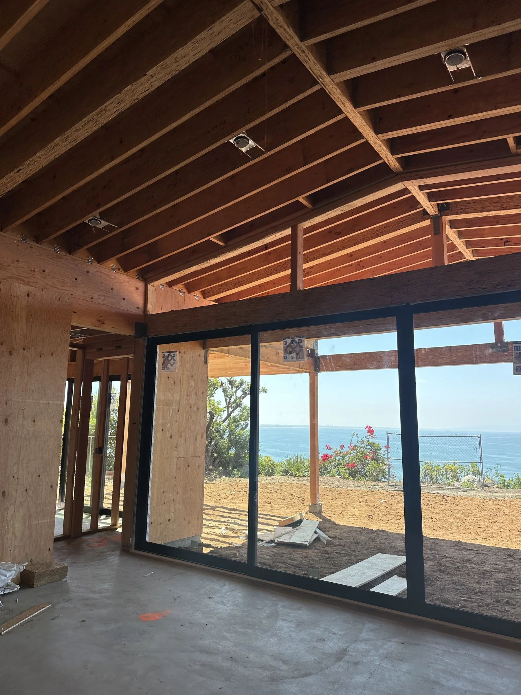 [new-construction] Ocean view through a black-framed glass wall in a Malibu home under construction
