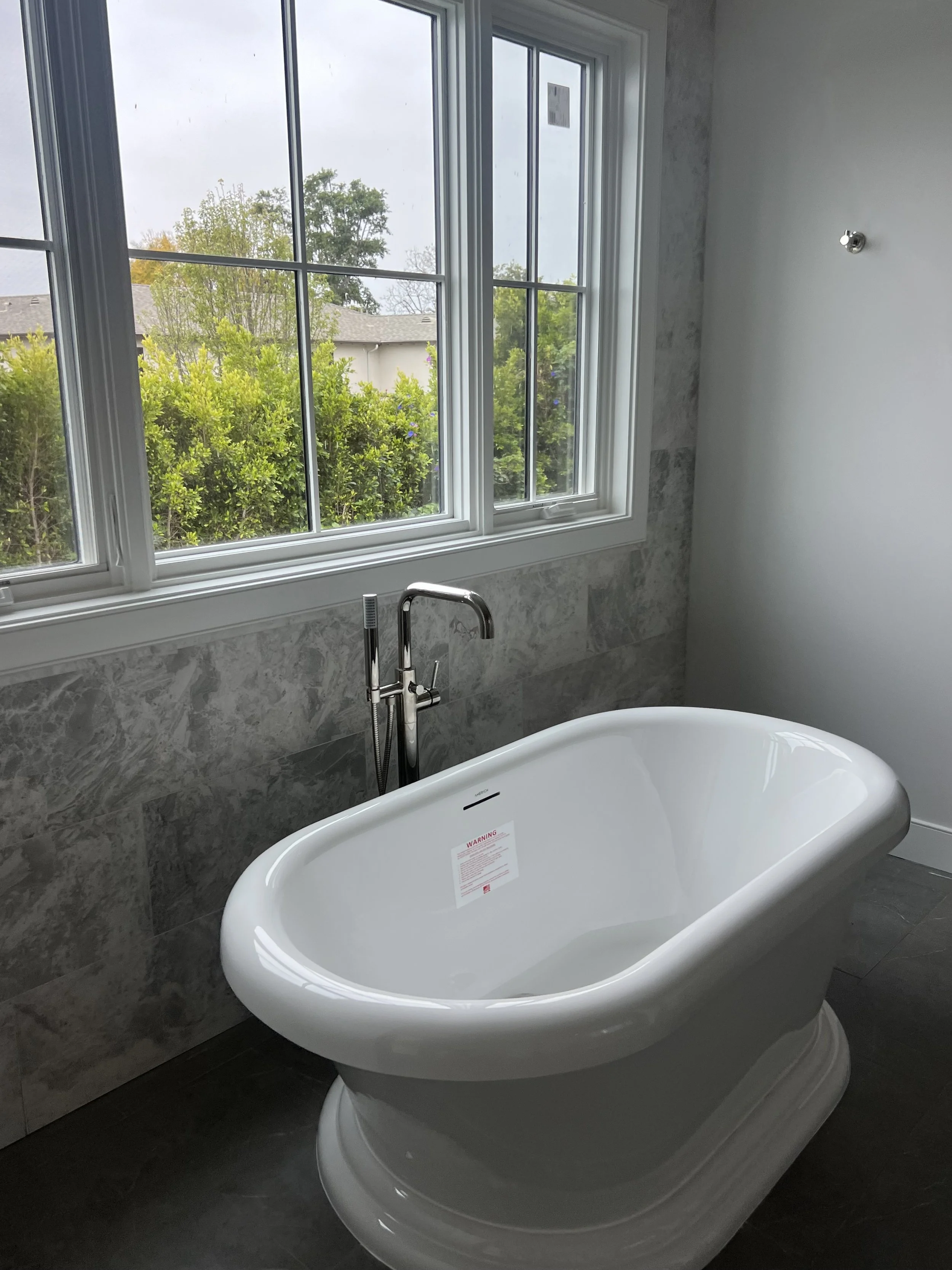 [bathroom-remodeling] Freestanding soaking tub beneath a triple window with grey marble walls and a floor-mounted tub filler, Rancho Park / West LA custom home