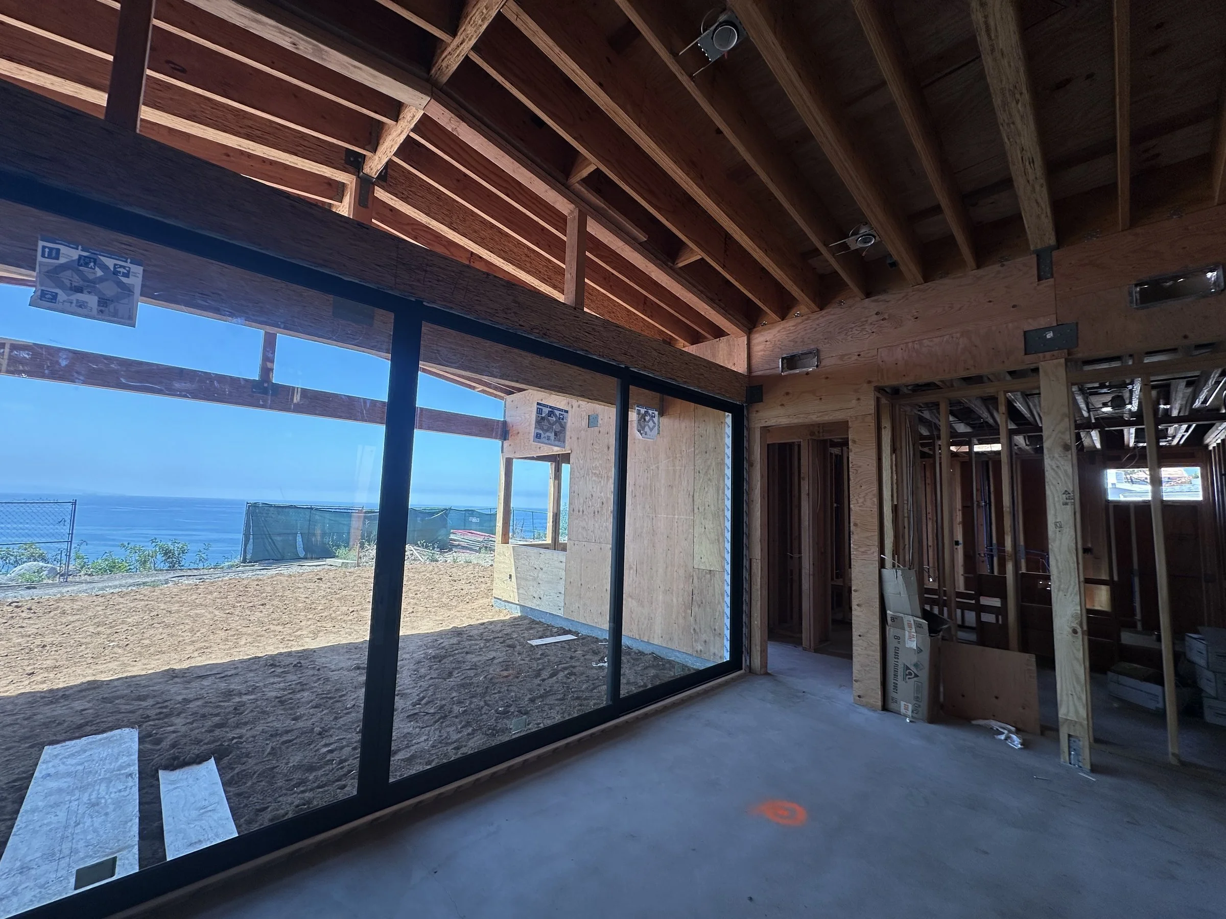 [new-construction] Framed great room with a black steel-framed glass wall opening to the ocean in Malibu