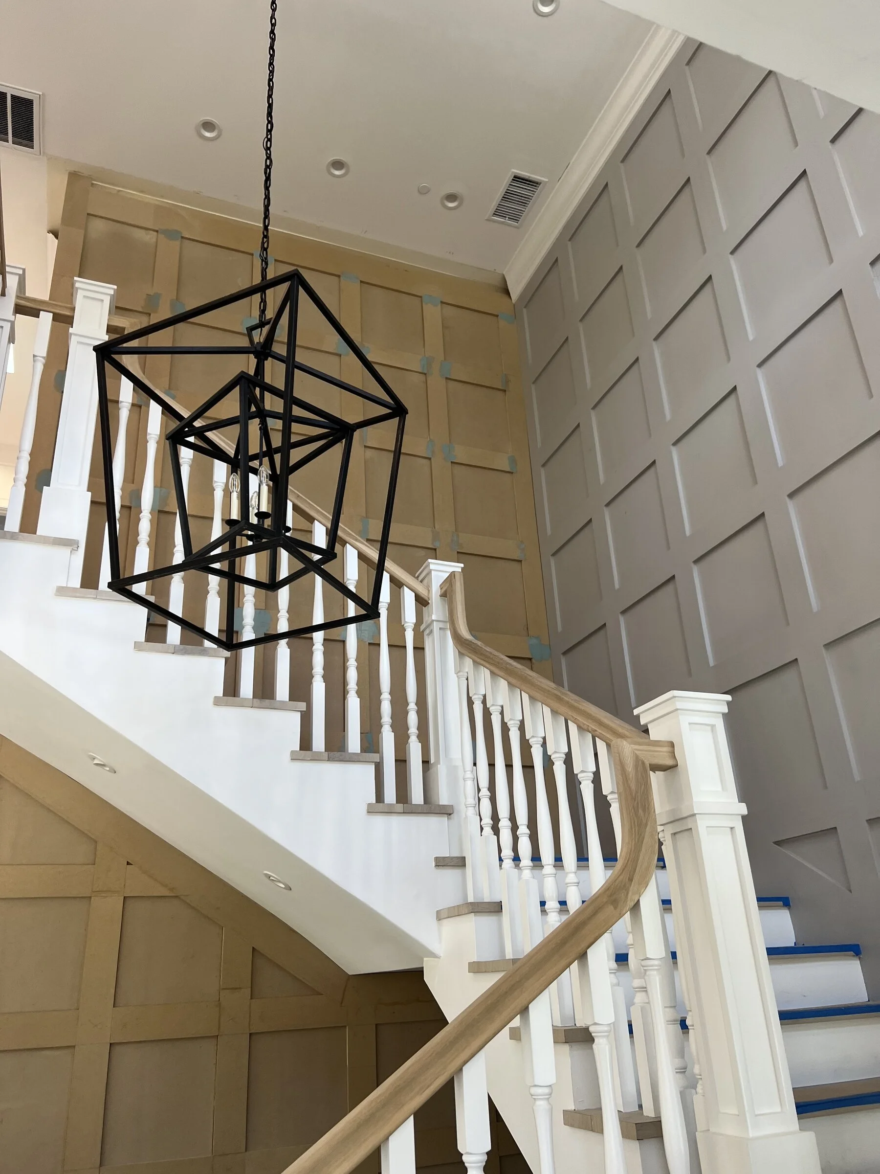 [home-additions] Custom curved staircase with a geometric statement chandelier and paneled wall in a Los Angeles home