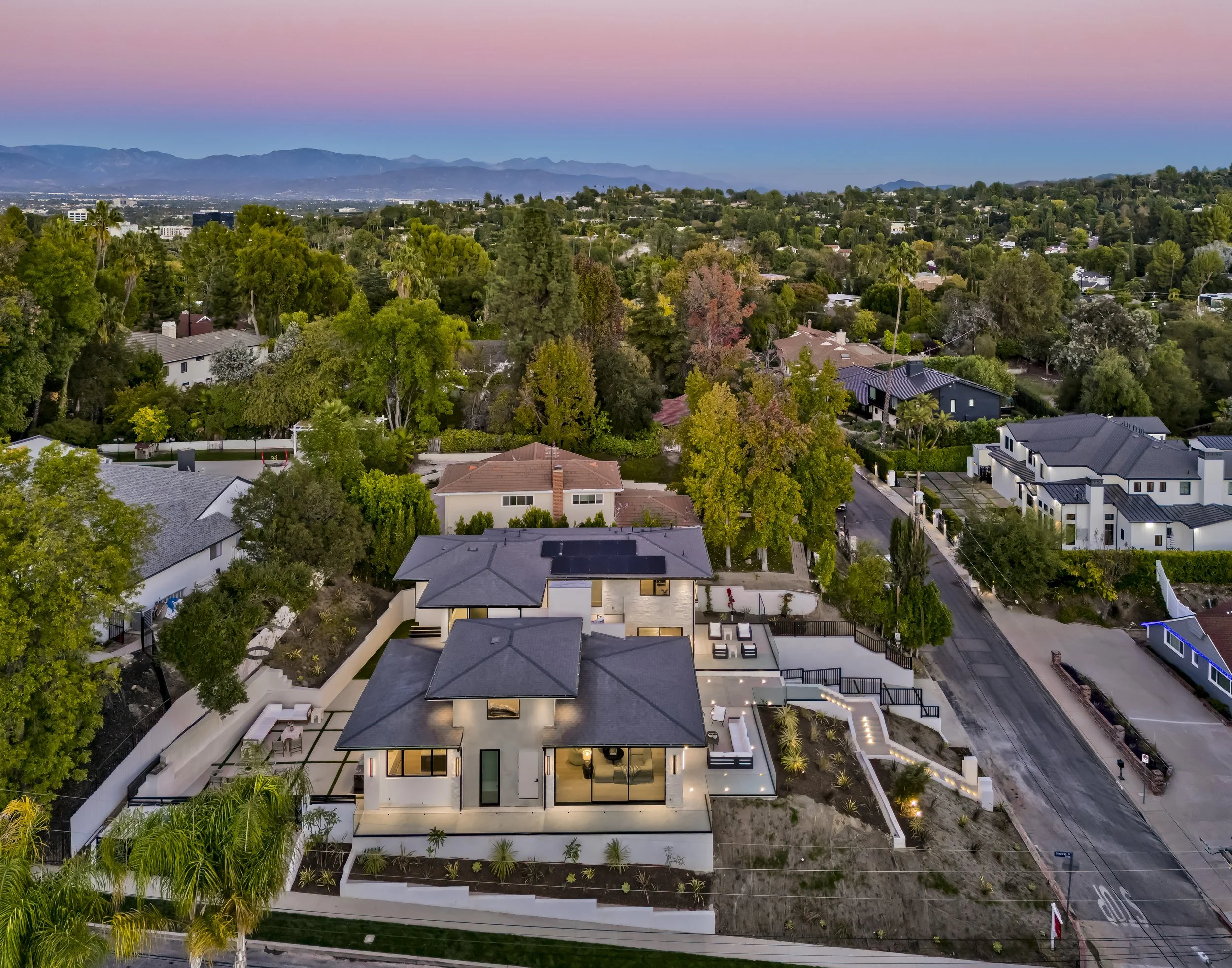Aerial twilight view of a modern Encino custom home with the San Fernando Valley and mountains beyond