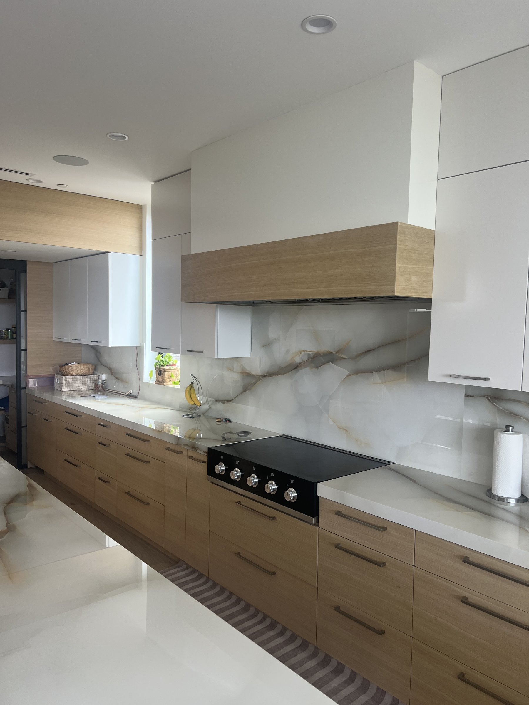 [kitchen-remodeling] Modern kitchen with a full-height onyx slab backsplash, white-oak cabinetry and an integrated cooktop in a Santa Monica home