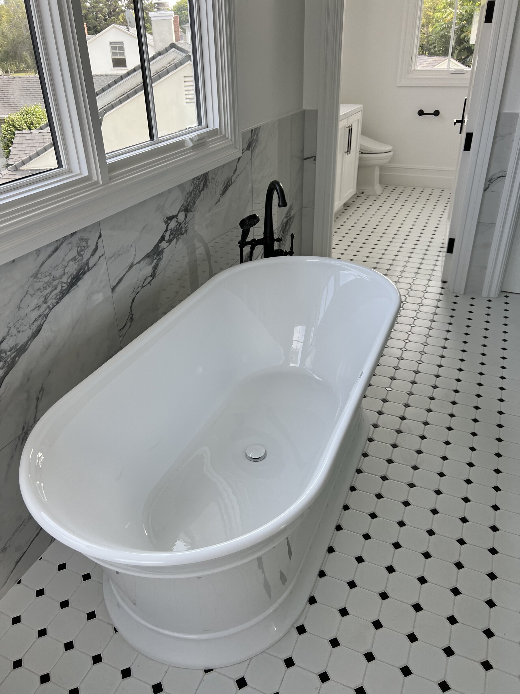 [bathroom-remodeling] Freestanding soaking tub with black floor-mount filler and marble wall in a Los Angeles master bathroom