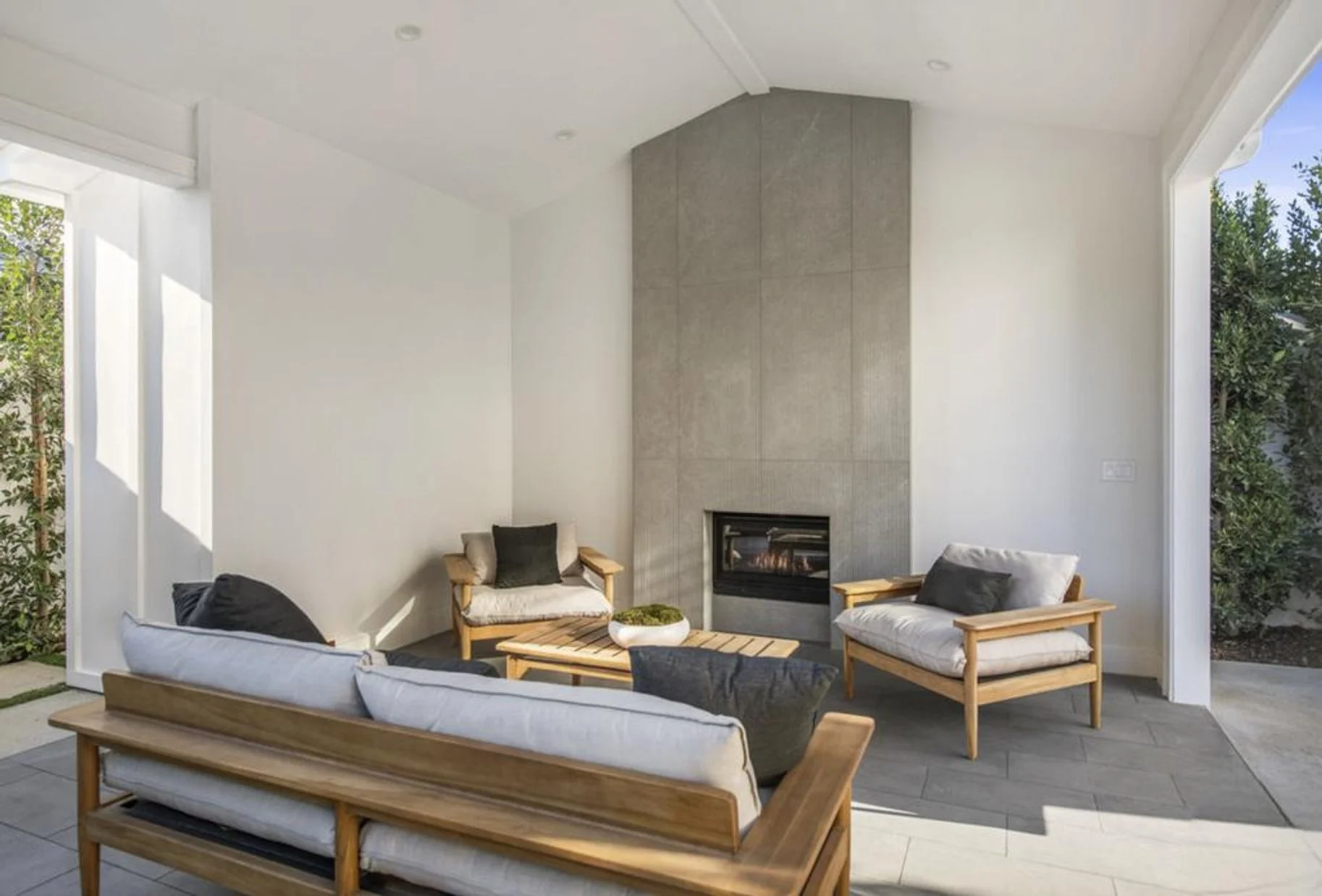 [hardscaping] Covered outdoor loggia with tiled fireplace and lounge seating opening to the yard, Brentwood custom home