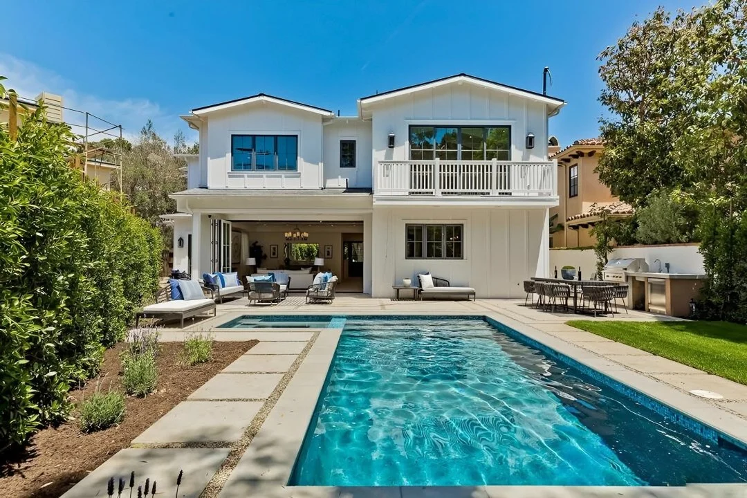Modern two-story white house with a backyard pool, outdoor seating area, and a barbecue grill, under a partly cloudy sky.