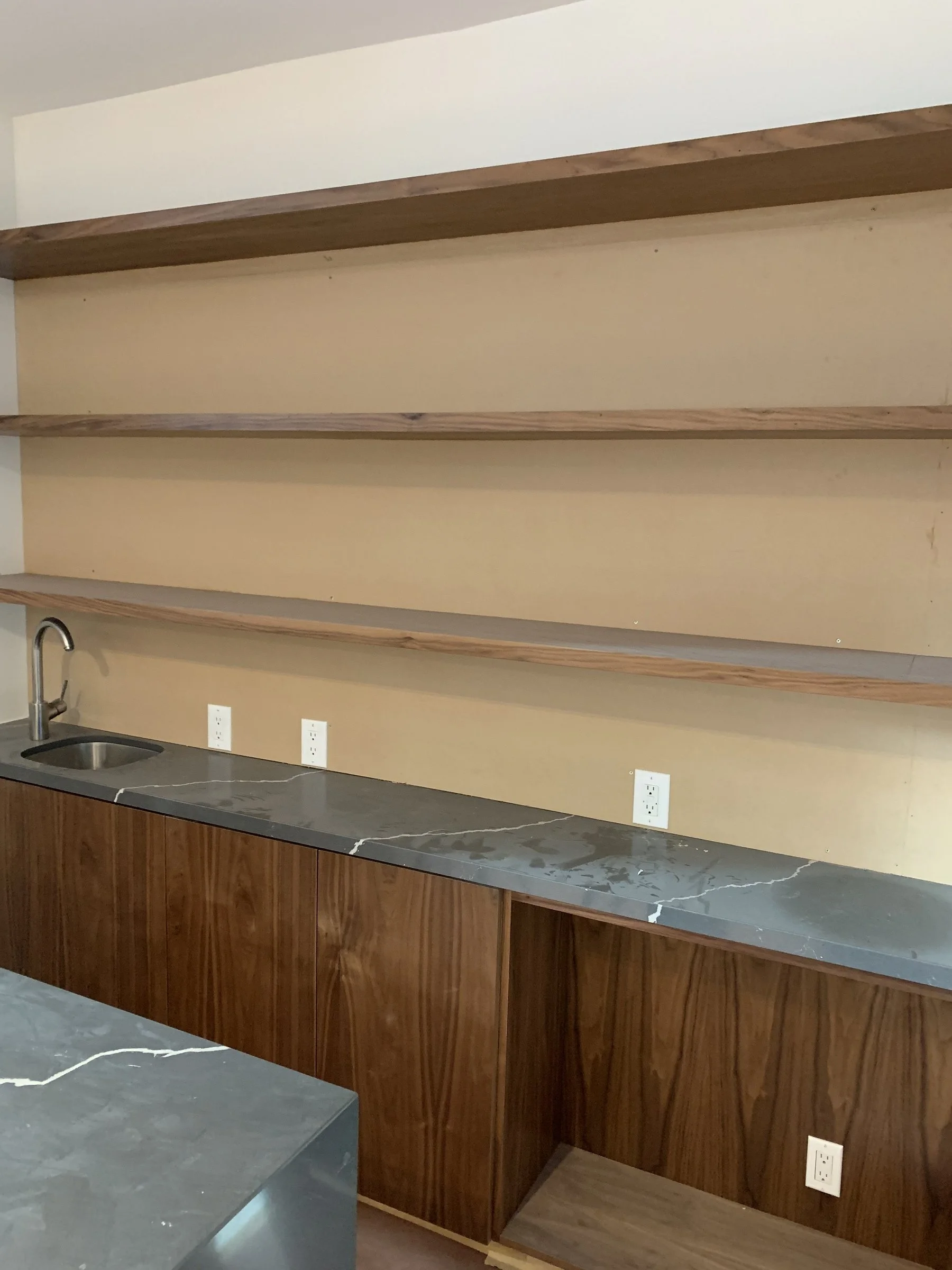 [kitchen-remodeling] Custom walnut floating shelves and cabinetry with a dark quartz counter and bar sink in Santa Monica
