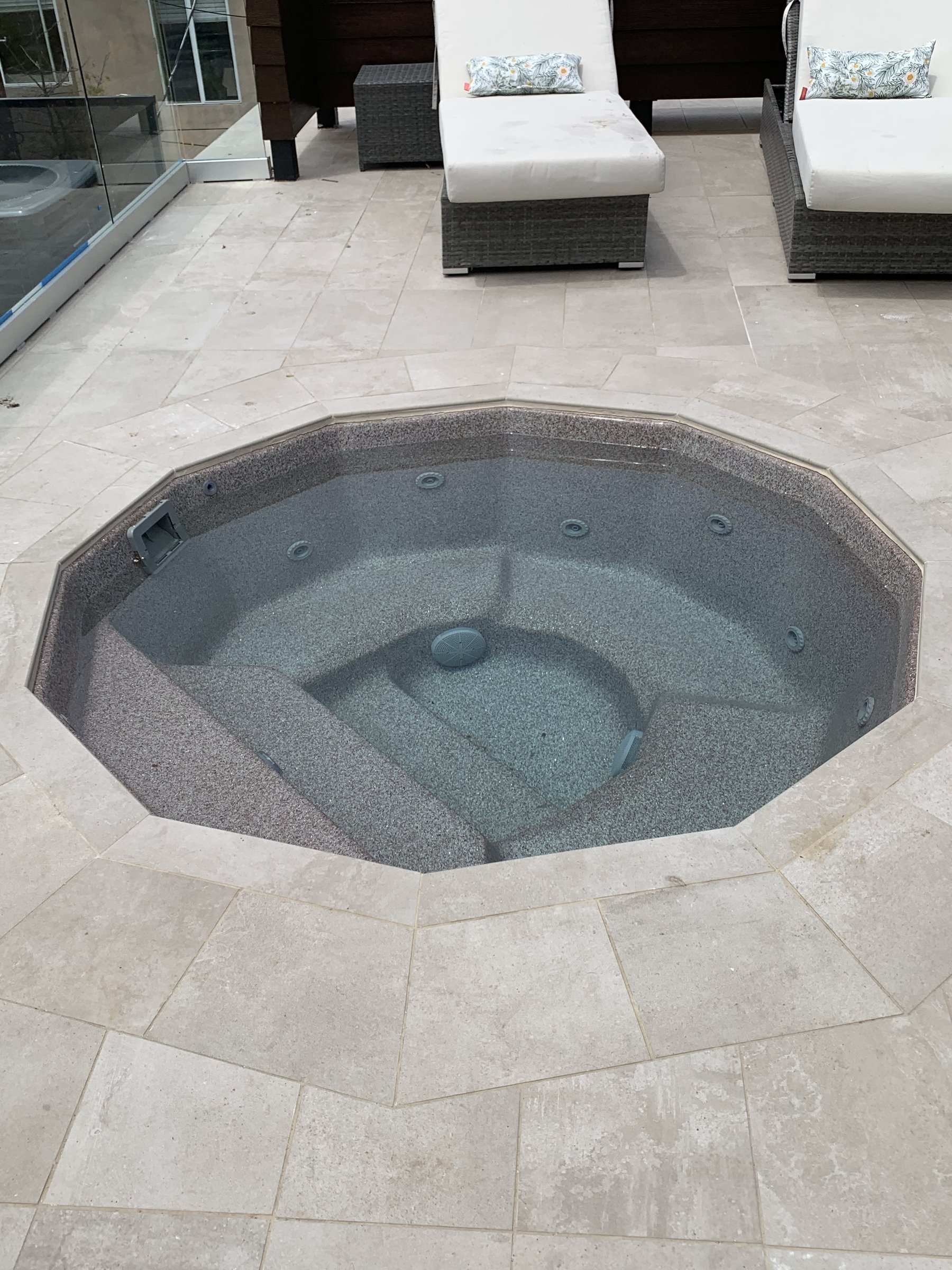 [hardscaping] Octagonal spa inset in a stone-tiled rooftop deck with glass railing and lounge seating in Santa Monica