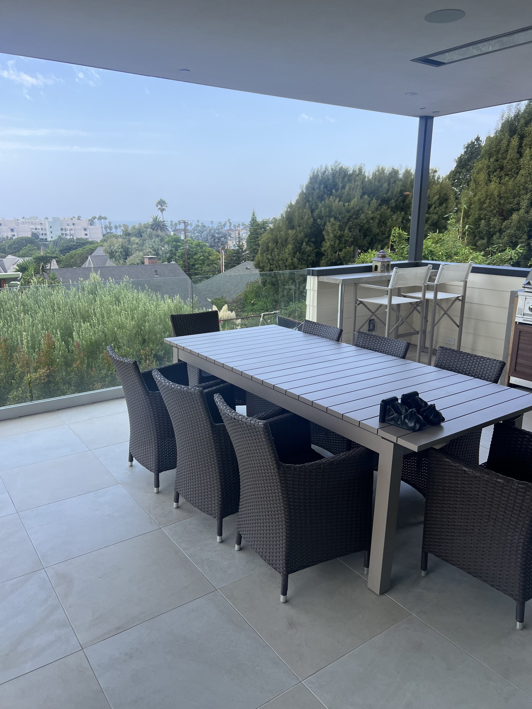 [hardscaping] Covered outdoor dining patio with an ocean view, built-in bar and frameless glass railing in a Santa Monica home