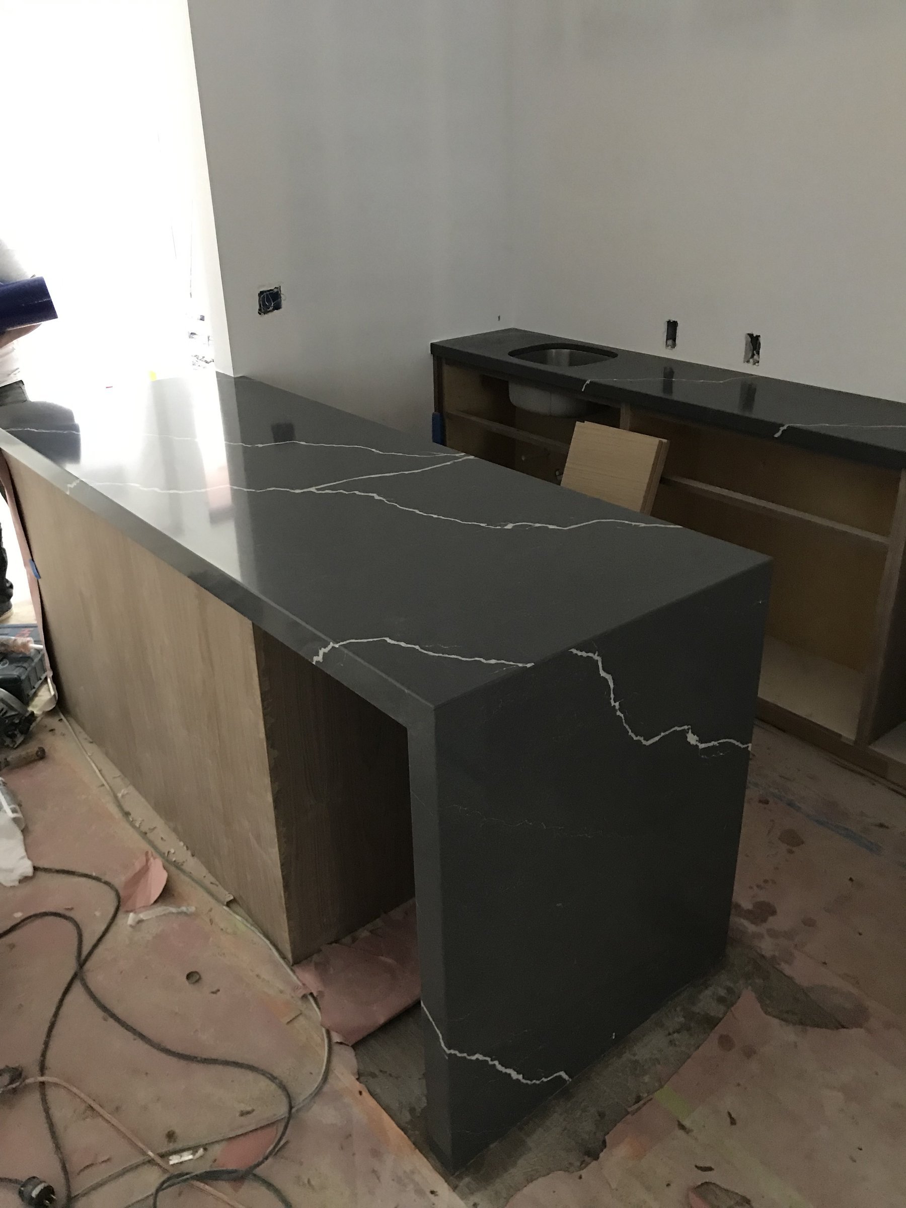 Dark quartz waterfall-edge island over walnut cabinetry under construction in Santa Monica