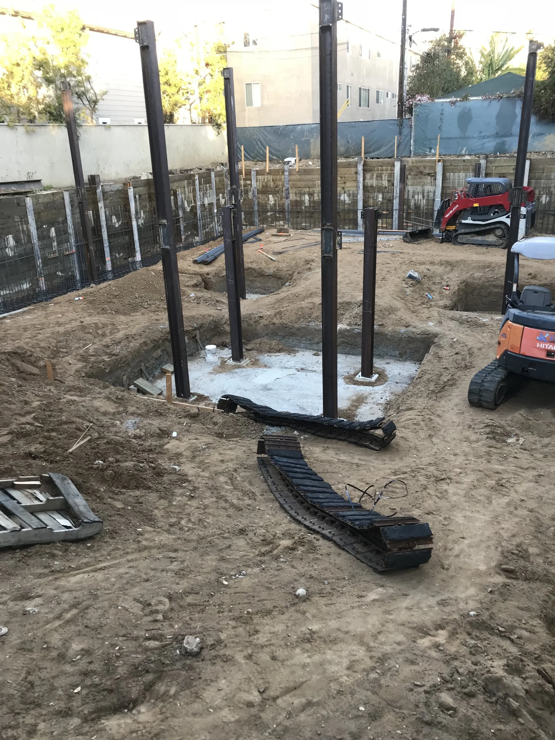 [new-construction] Structural steel columns set on concrete footings in an excavated pad at golden hour in Santa Monica