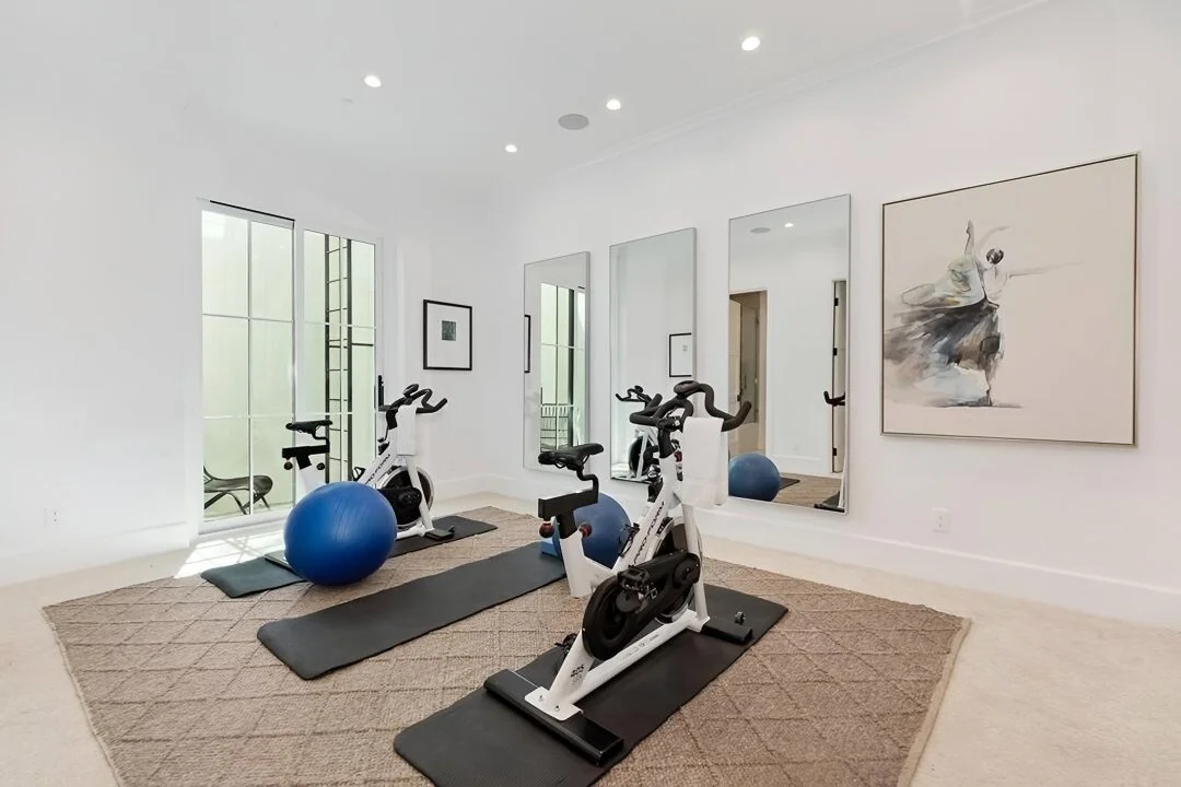 [home-additions] Home gym with spin bikes, mirrored wall, and large-scale art in a Cheviot Hills custom home