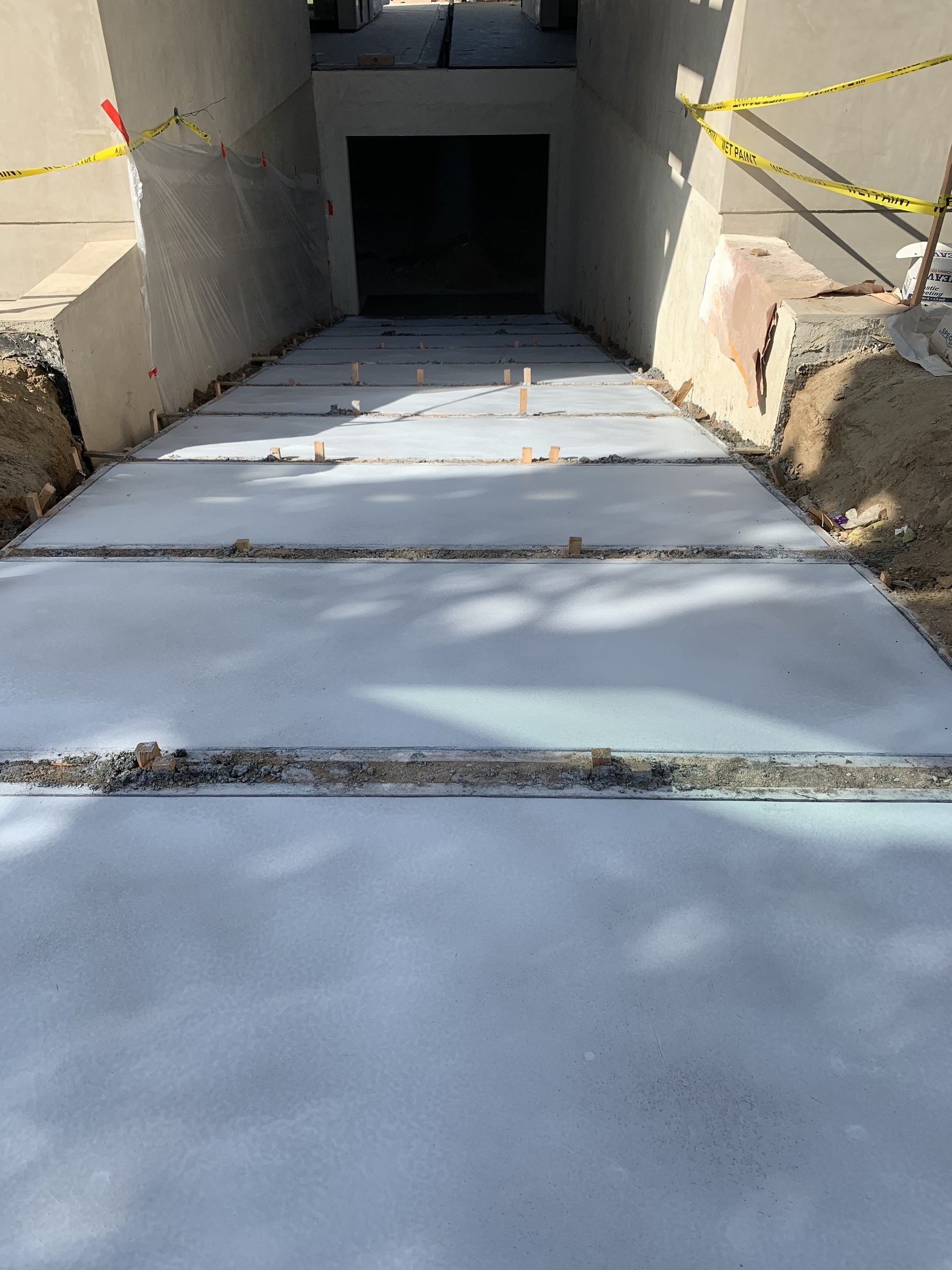 [hardscaping] text  Freshly finished concrete walkway between stucco walls on a Santa Monica build