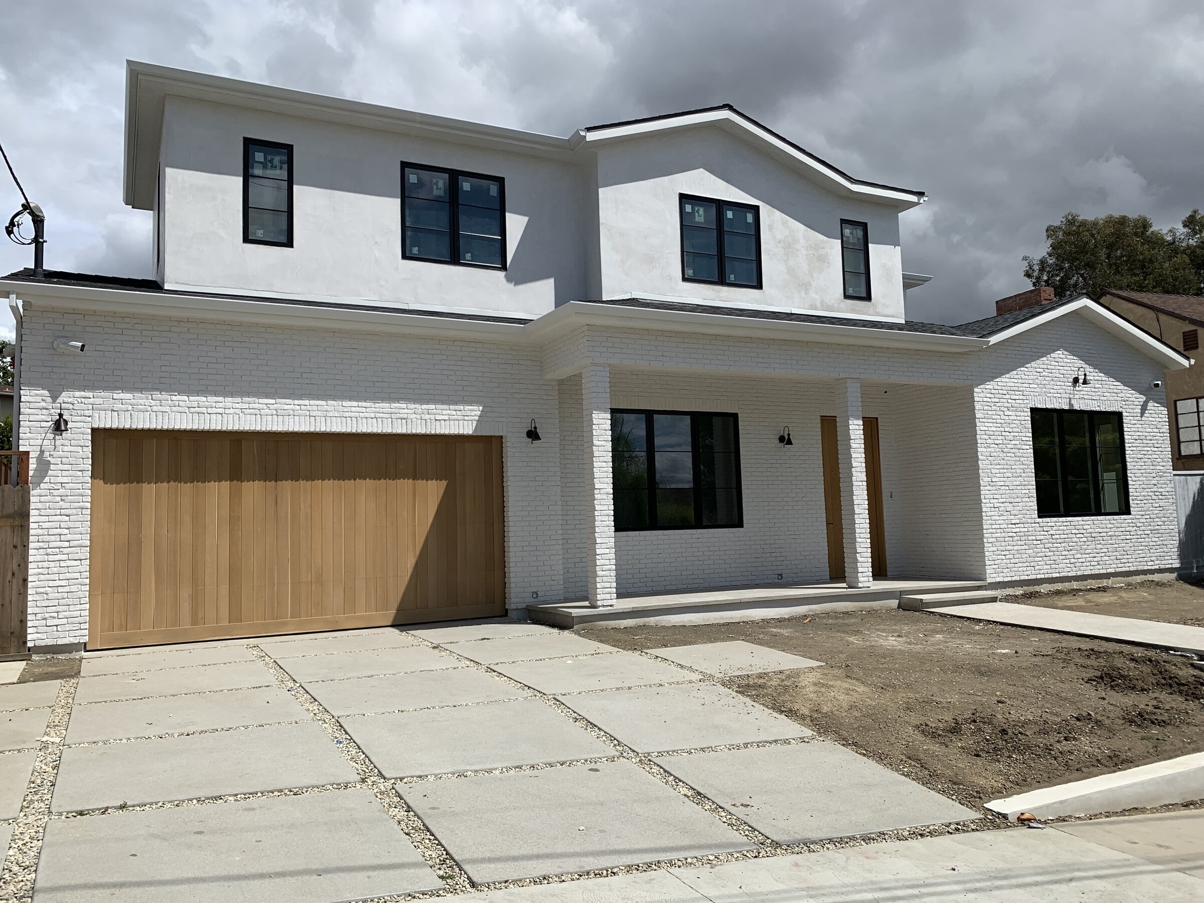 Finished white painted-brick and stucco modern farmhouse front exterior with a wood garage in Los Angeles