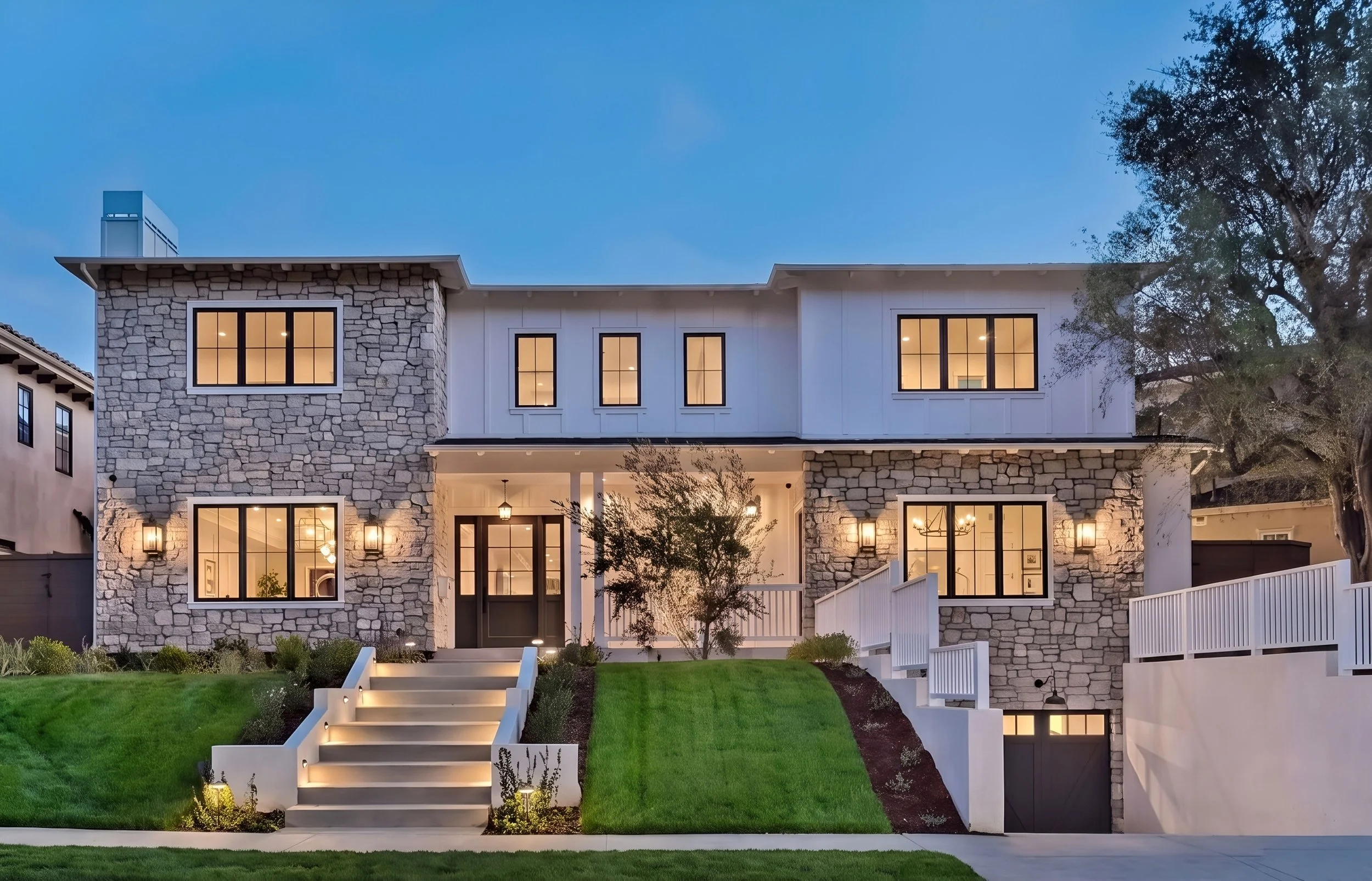 Modern two-story house with large glass windows, a backyard swimming pool, outdoor seating area, and lush greenery including palm trees in the background