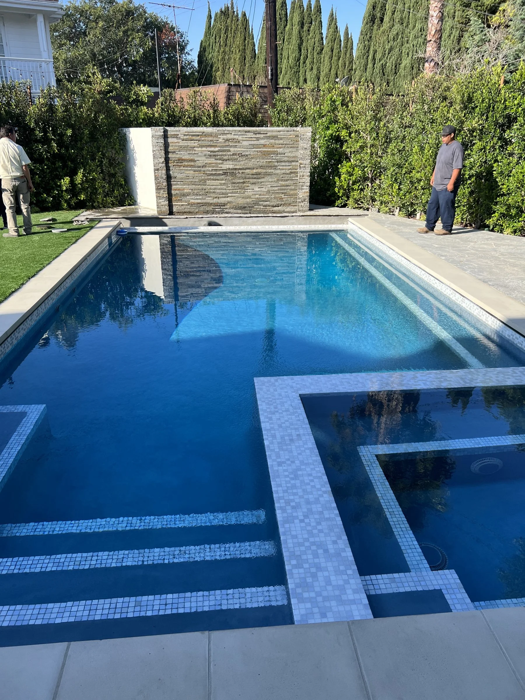 [pool-installation] Finished custom pool and spa with glass-tile steps and a stone water wall in Los Angeles