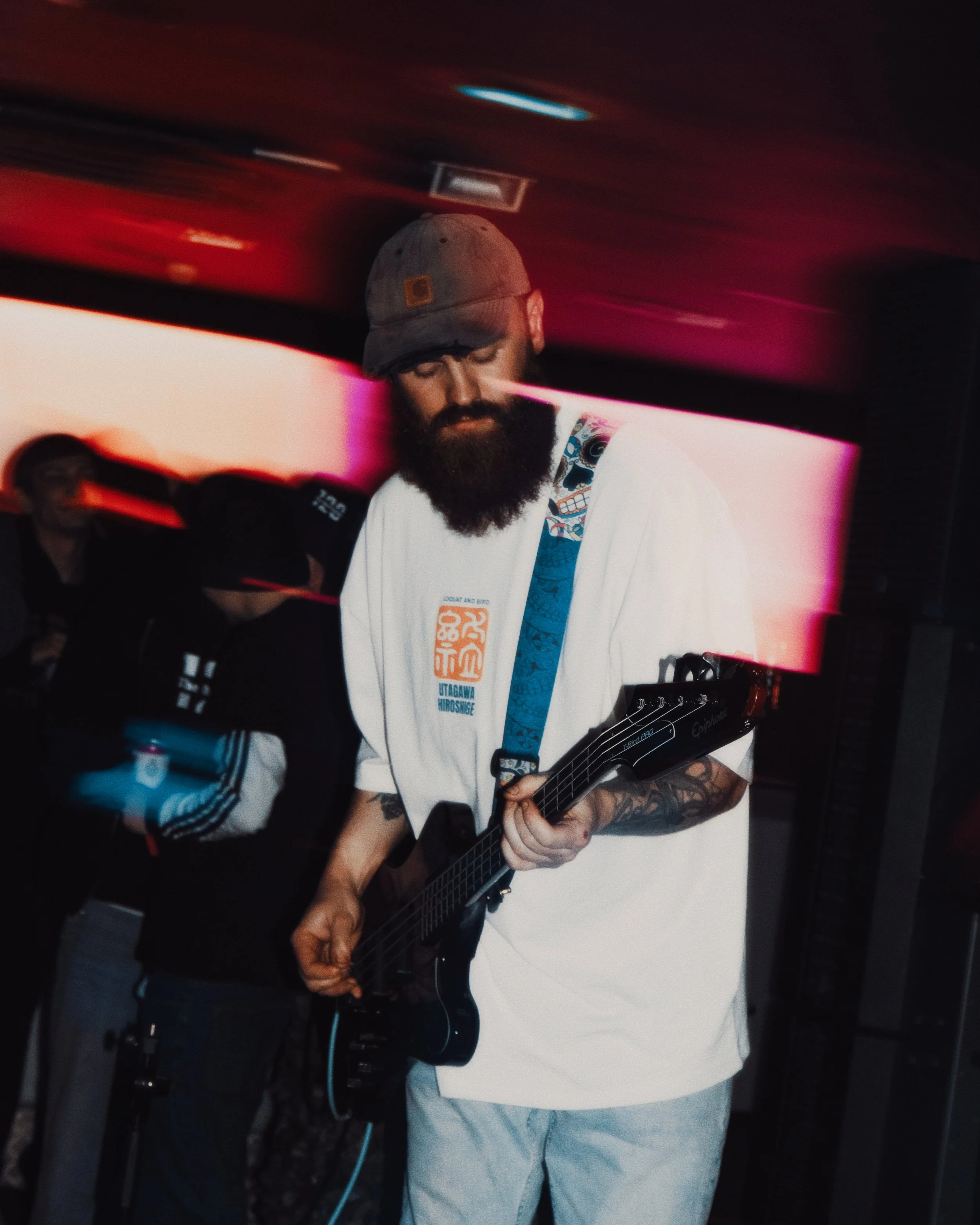 A white male with a large brown bear wearing a cap plays bass guitar at a gig