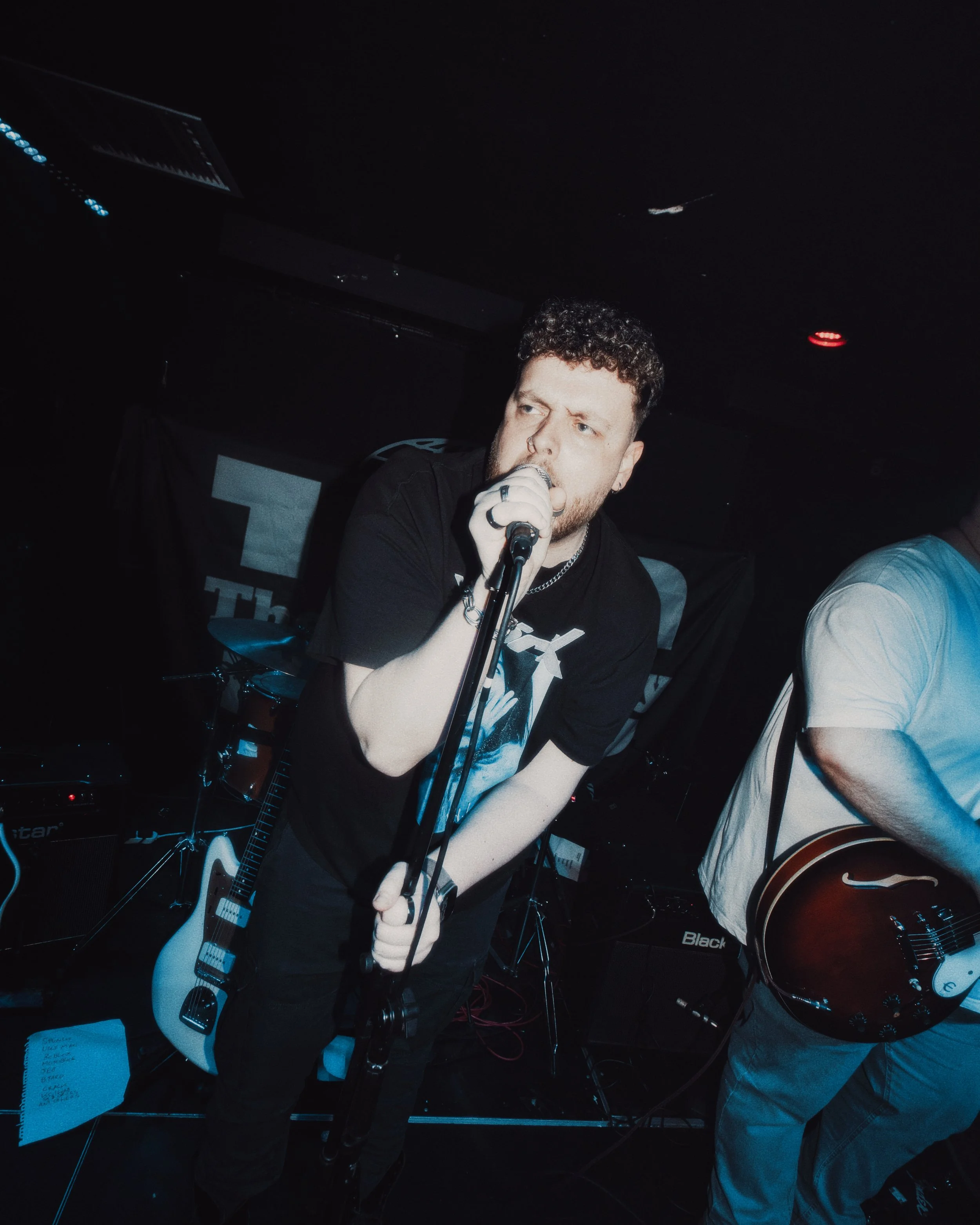A white male with brown curly hair leaning over a microphone singing during a gig