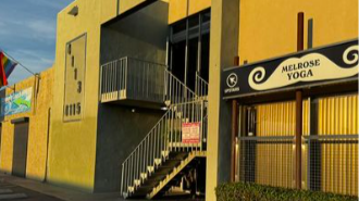 Exterior of a yoga studio named Melrose Yoga, with an external staircase and yellow building facade.