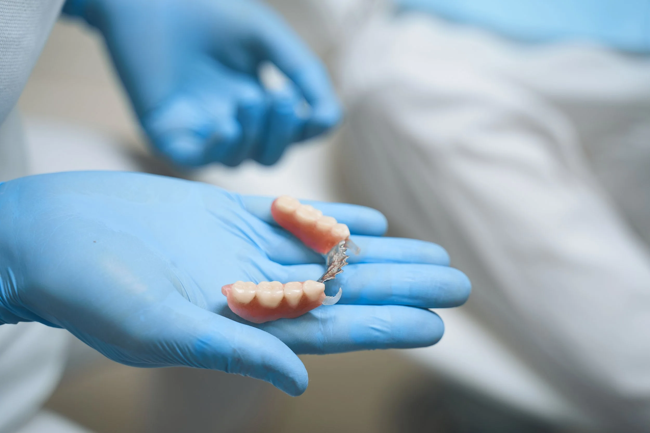 A dentist wearing blue gloves holding a set of artificial teeth.