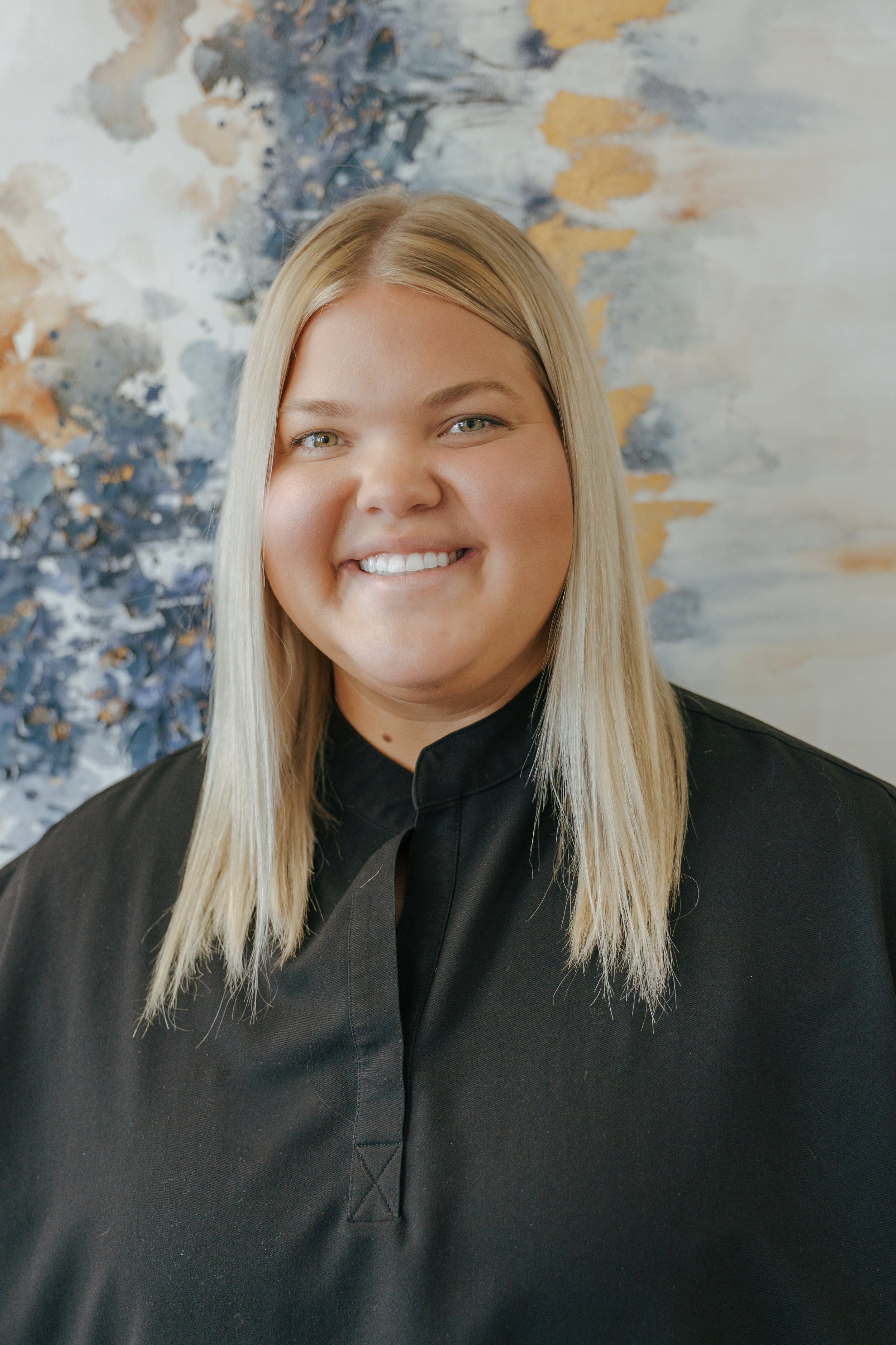A woman with blonde hair smiling in front of an abstract floral painting.