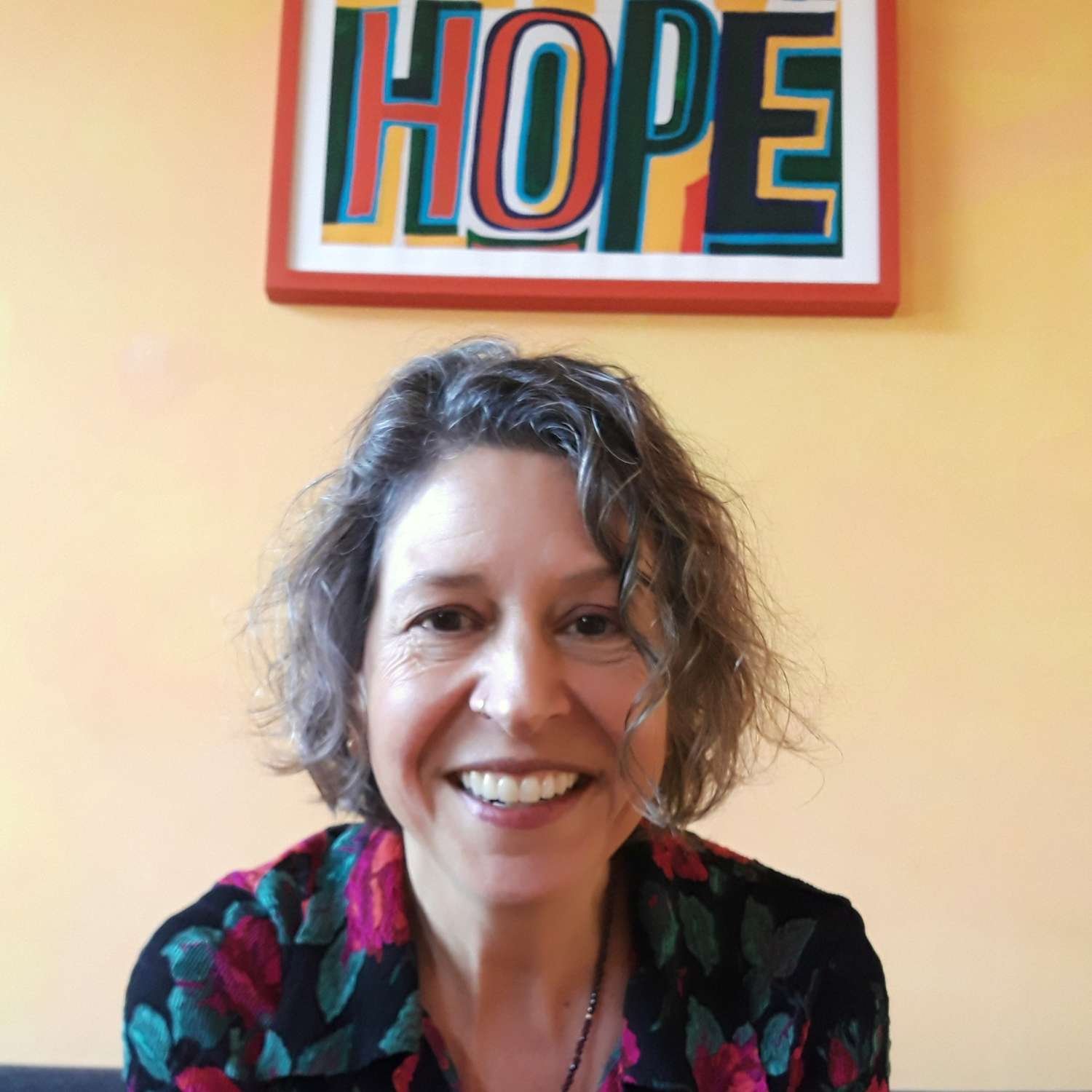 The author's headshot, smiling and seated before a colourful print reading 'HOPE'.