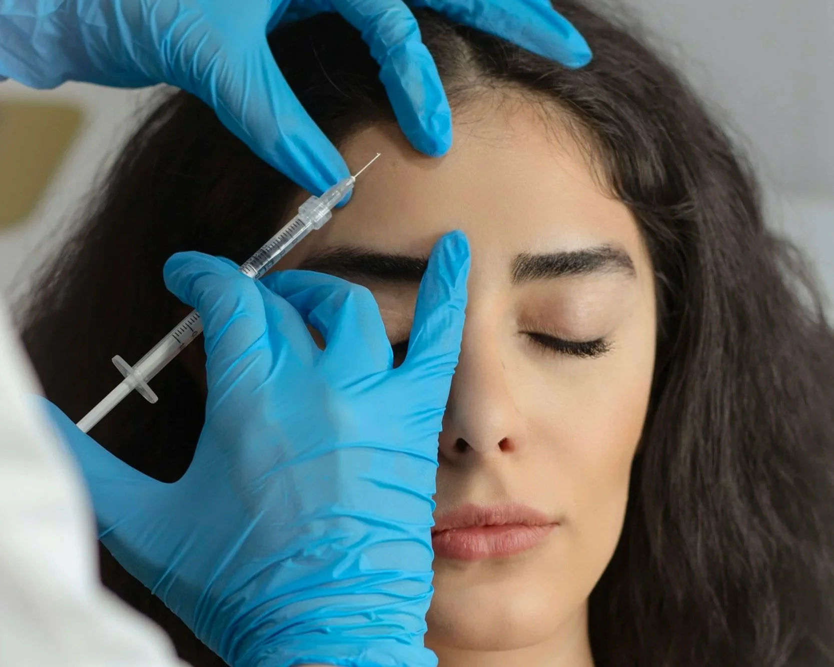 Person receiving a cosmetic injection in her forehead from a medical professional wearing blue gloves.